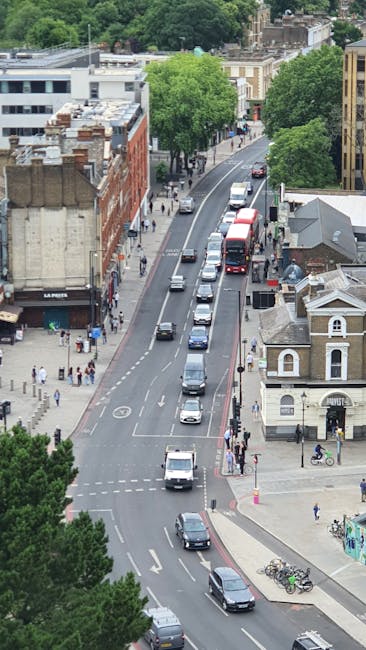 View of a street scene in Clapham with a brick building featuring large arched windows and a clock mounted on a pole. A blue train carriage with yellow 'CADDIN LOCK' branding is positioned across the 